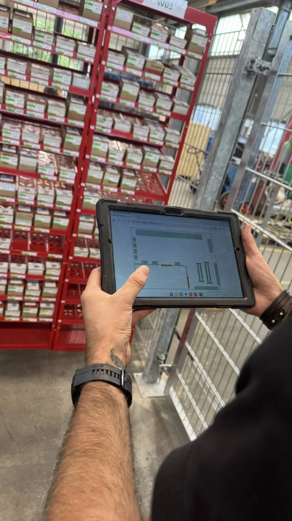 Mitarbeiter bedient die Lageransicht auf dem Tablet direkt an der Regalreihe